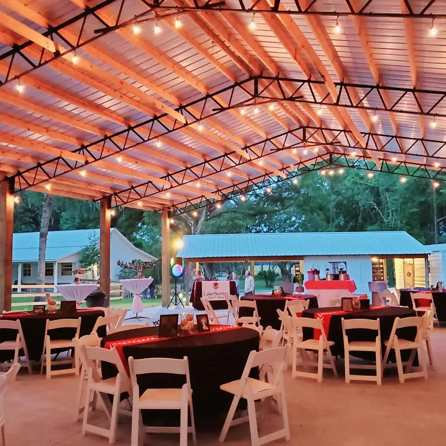 The pavilion set for an evening reception, warm lights overhead and tables in deep red