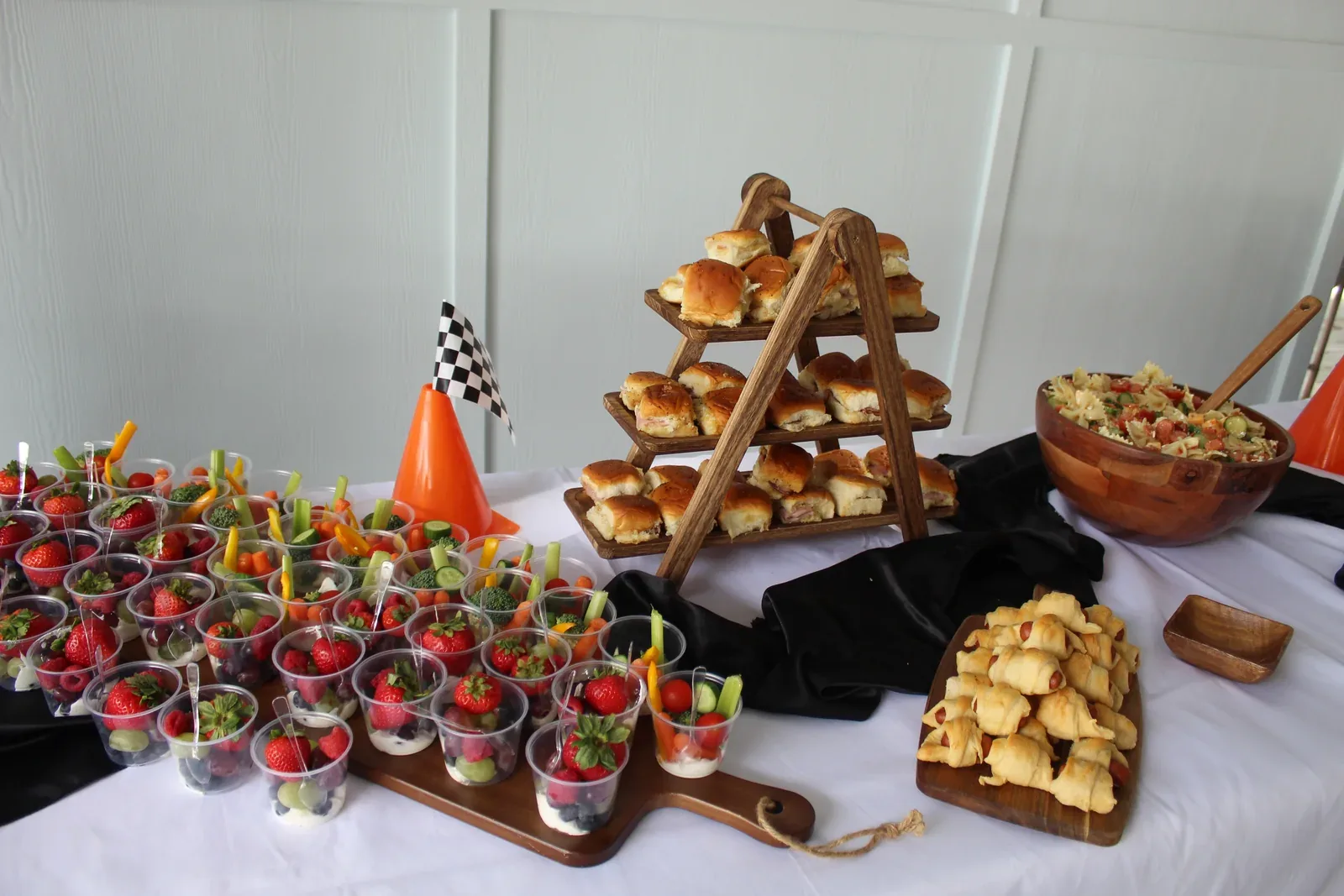 A party food spread on a black cloth, with tiered stands of pastries and fruit cups