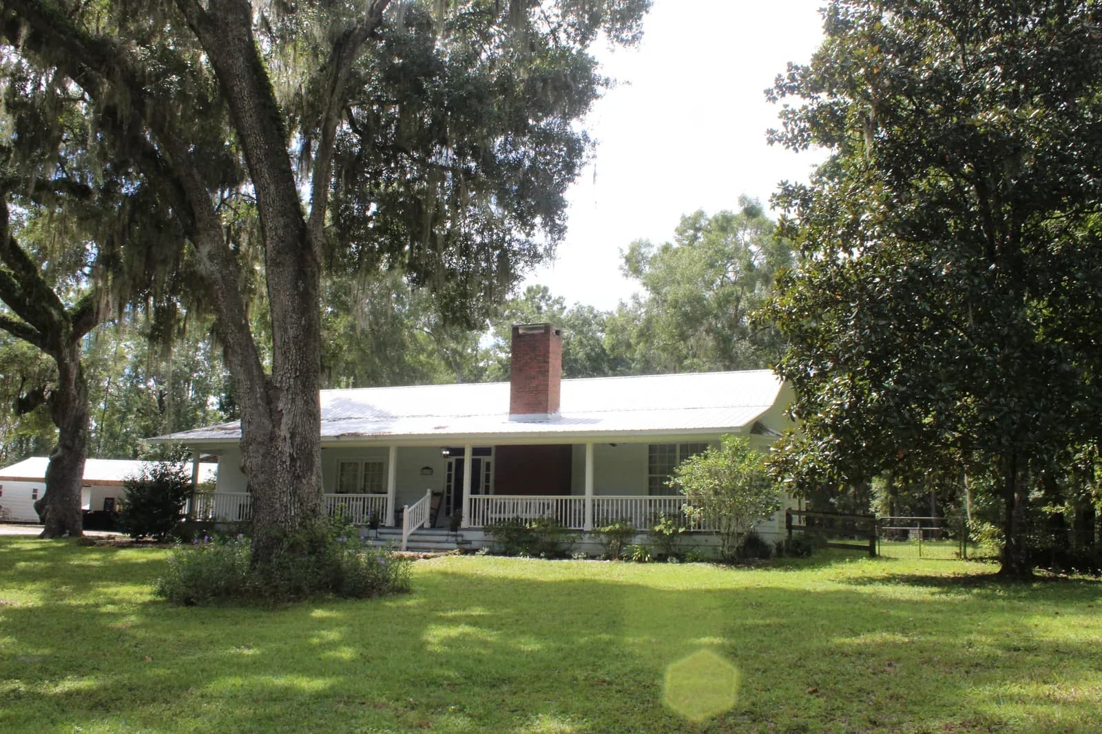 The white farmhouse on the property, seen across the lawn through the trees